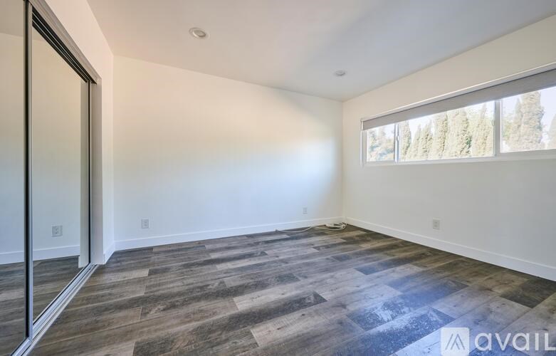 A room with a wooden floor and a window showing trees outside.