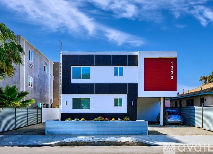 A modern house with a red garage door is surrounded by a fence and has a clear blue sky above.