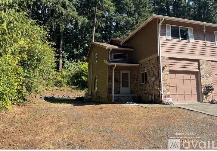 A house with a brown siding and a white door is surrounded by trees.