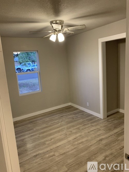 A room with a ceiling fan and light, wooden flooring, and a window showing an outdoor scene.