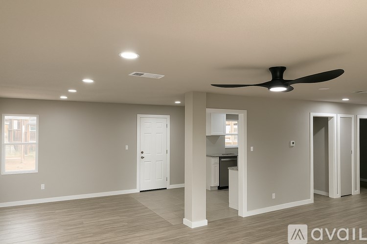 A spacious room with a ceiling fan and a kitchen area in the background.