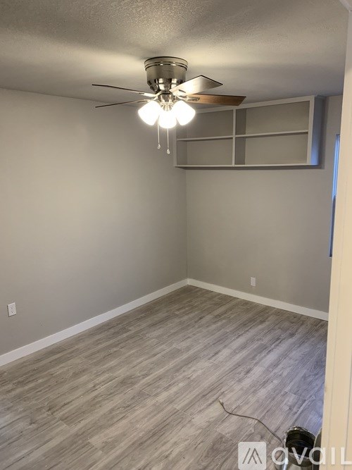 A room with a ceiling fan and light fixture, and a wooden floor.