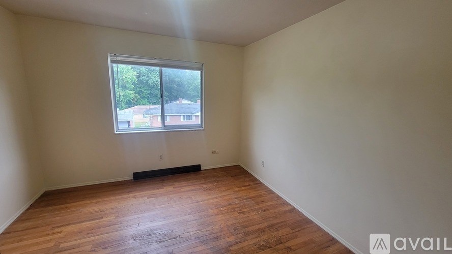 A room with wooden flooring and a window showing a view of a house.