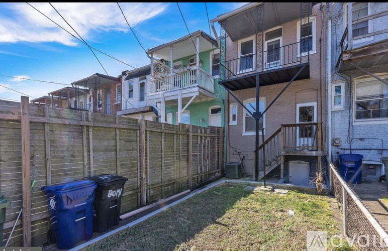 A backyard with a fence and a blue trash can.