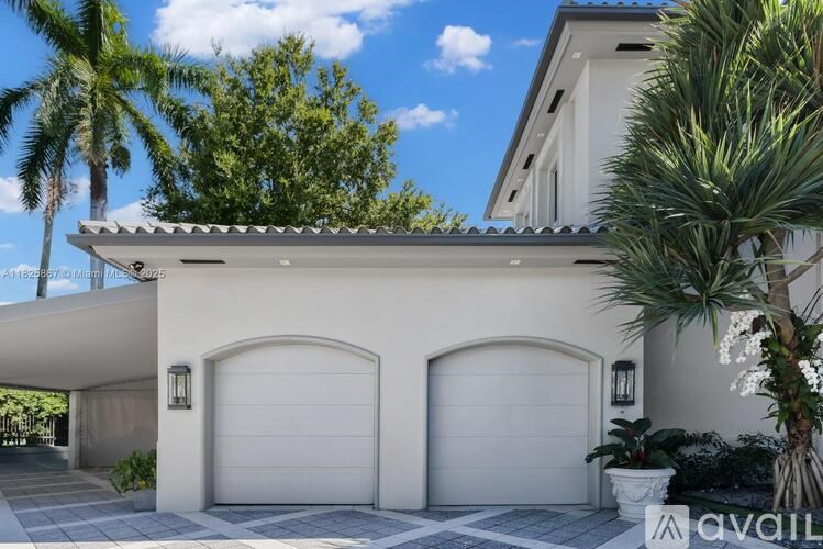 A white house with two garage doors and a palm tree in front.