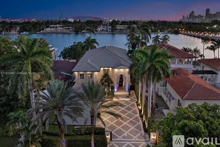 A house with a large front yard and palm trees in front of a body of water.