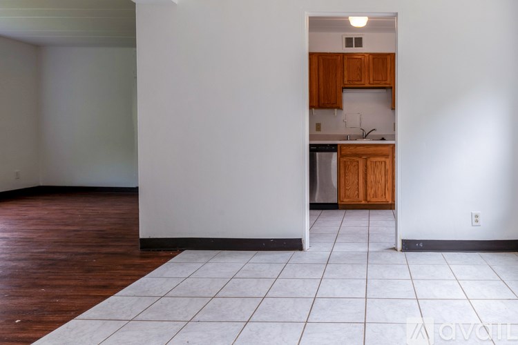A kitchen with wooden cabinets and a black fridge is visible from a hallway.