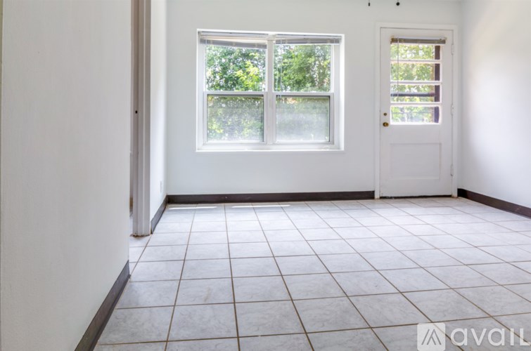 A room with a white door and a window with a view of trees.