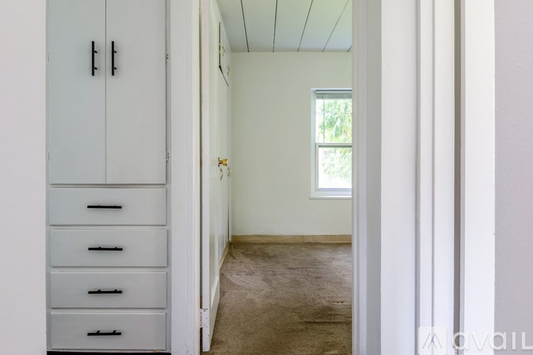A white cabinet with drawers is next to a doorway leading to a carpeted room.