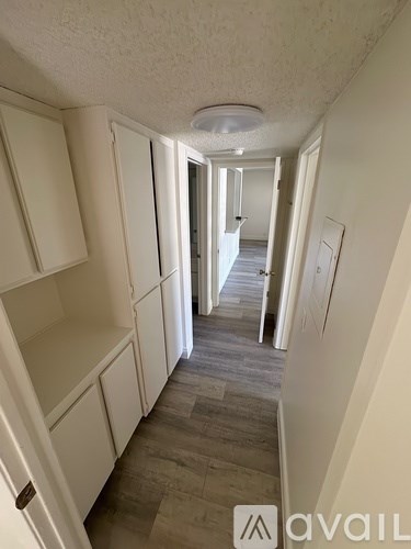 A narrow hallway with white walls and a wooden floor.