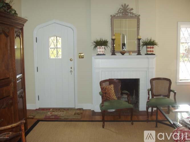 A white door with a glass window is flanked by two chairs and a fireplace.