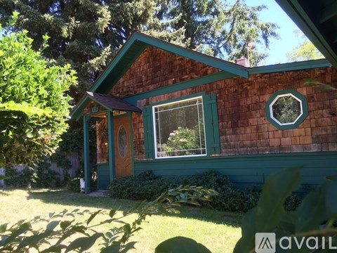 A house with a green door and window is surrounded by trees.