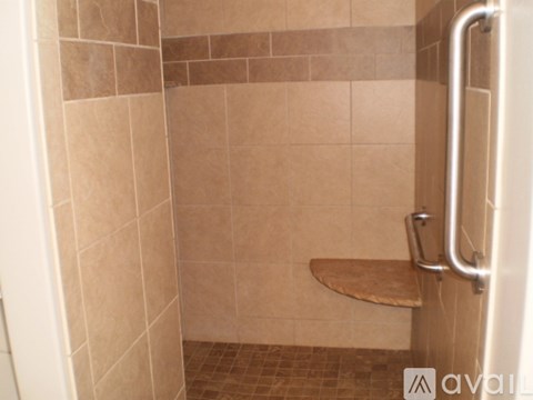 A tiled shower with a bench seat and grab bar.
