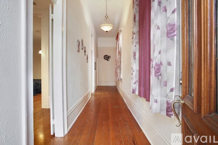 A hallway with a white door on the left and a window with purple curtains on the right.