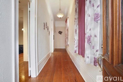 A hallway with a white door on the left and a window with purple curtains on the right.