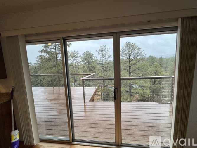 A sliding glass door with a view of a deck and trees outside.
