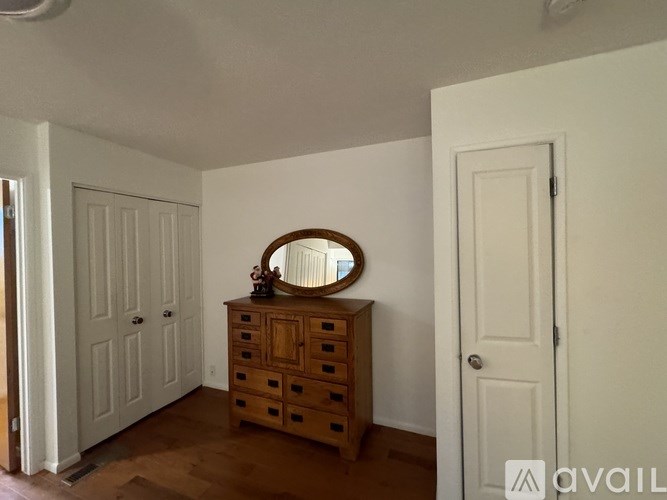 A wooden dresser with a round mirror on top is in a room with white walls.