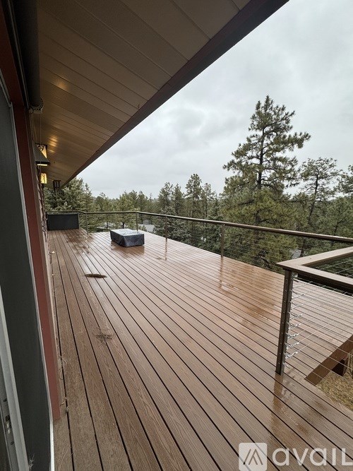 A wooden deck with a metal railing and a view of trees in the distance.