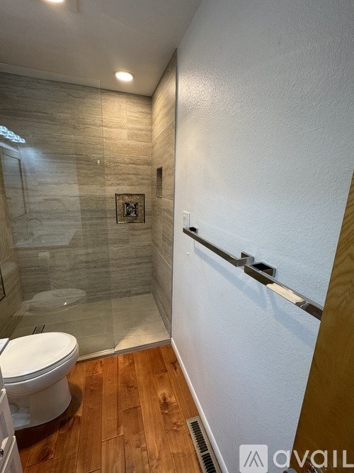 A bathroom with a toilet, a glass shower stall, and a wooden floor.