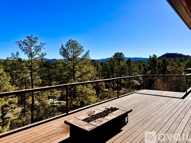 A wooden deck with a bench overlooks a forest.