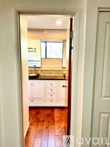 A kitchen with wooden floors and white cabinets is visible through an open door.