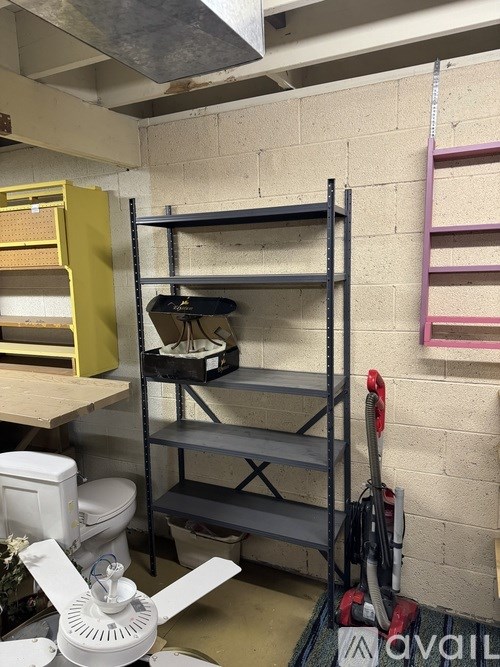 A room with a fan, a shelf, and a vacuum cleaner.