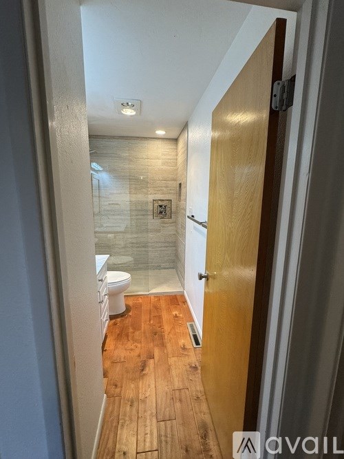 A hallway with a toilet and a shower in the background.
