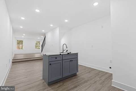 A kitchen island with a sink is in the middle of a room with white walls and wood flooring.