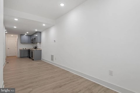 A brightly lit empty room with wooden flooring and white walls.