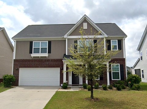 A two-story house with a garage and a tree in front.