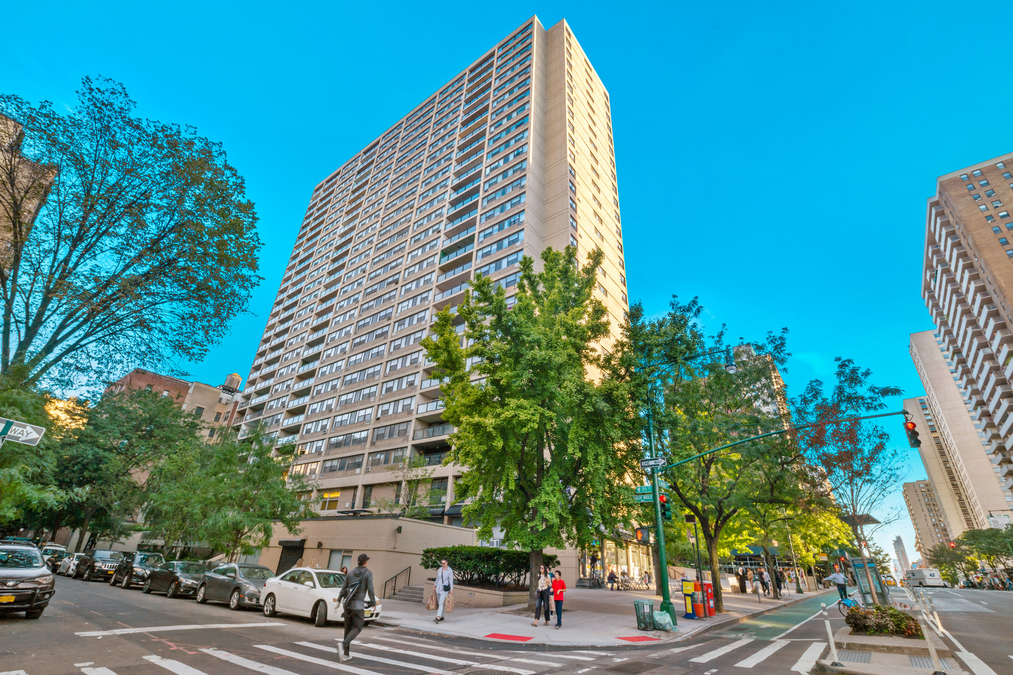 A tall building is surrounded by trees and cars on the street.