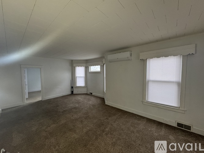 A spacious room with carpeted floor, two windows, and a door leading to another room.