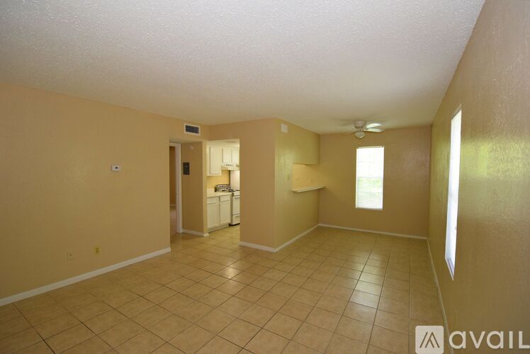 A room with beige walls and tiled flooring, with a doorway leading to another room.
