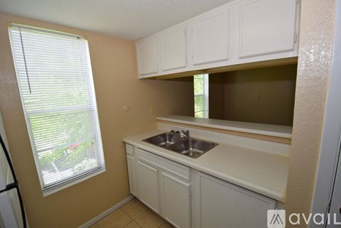 A kitchen with white cabinets and a window with blinds.