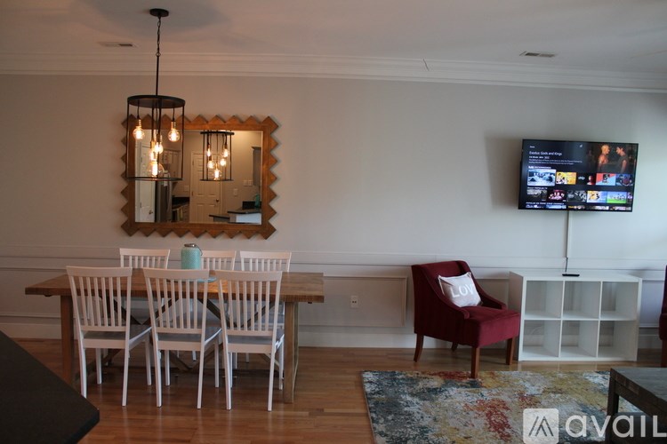 A living room with a wooden table and chairs, a mirror, a TV, and a rug.