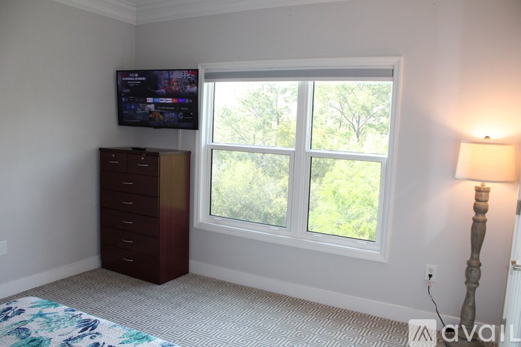 A room with a television on the wall and a window with a view of trees outside.