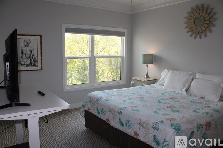 A bedroom with a bed, a table, a television, and a window.