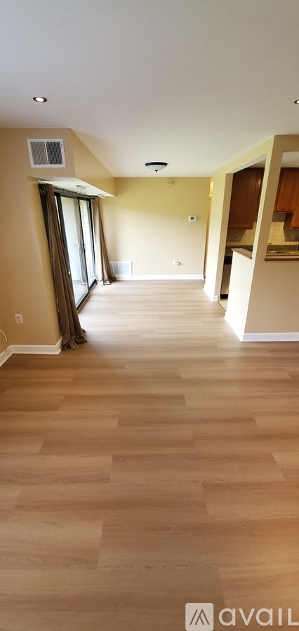 A spacious room with wooden flooring and a window with curtains.