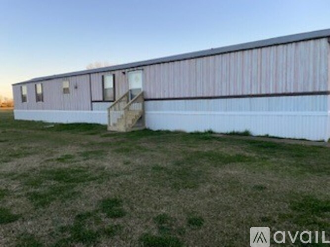A long building with a white and pink exterior sits in a grassy field.
