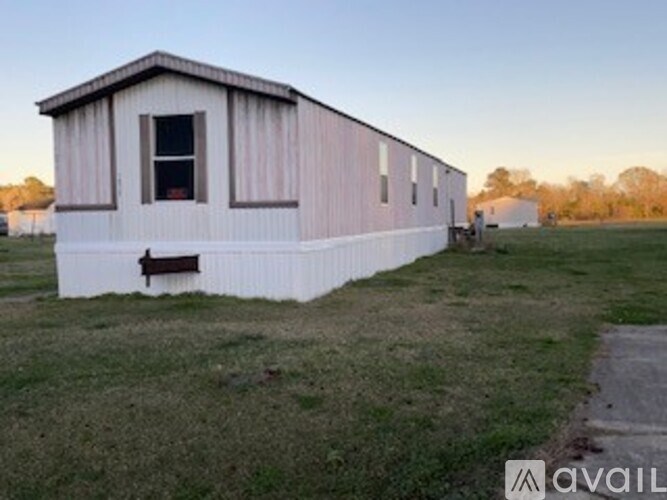 A small white building with a brown door sits in a grassy field.