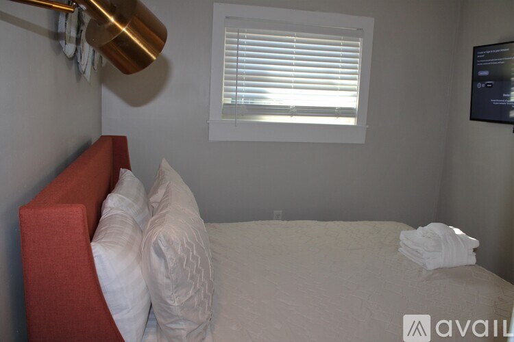 A bedroom with a bed, a red headboard, and a window with blinds.