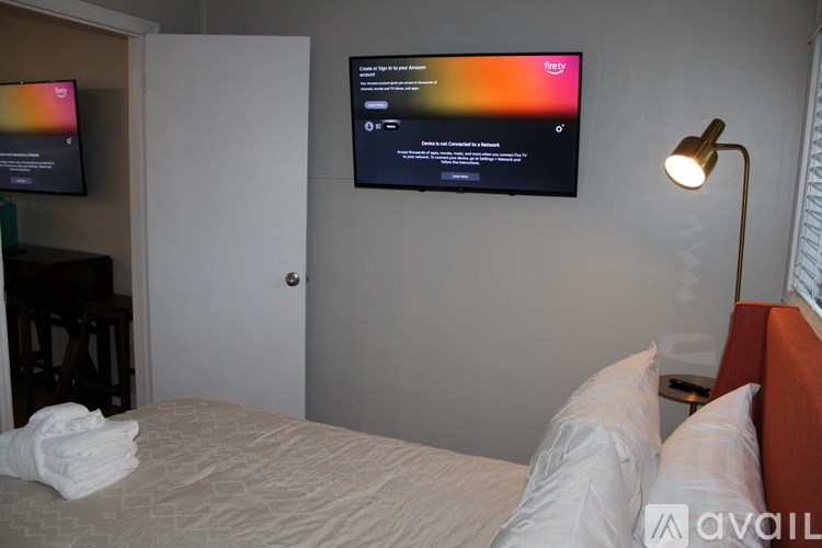 A bedroom with a bed, a lamp, and a flat screen TV mounted on the wall.