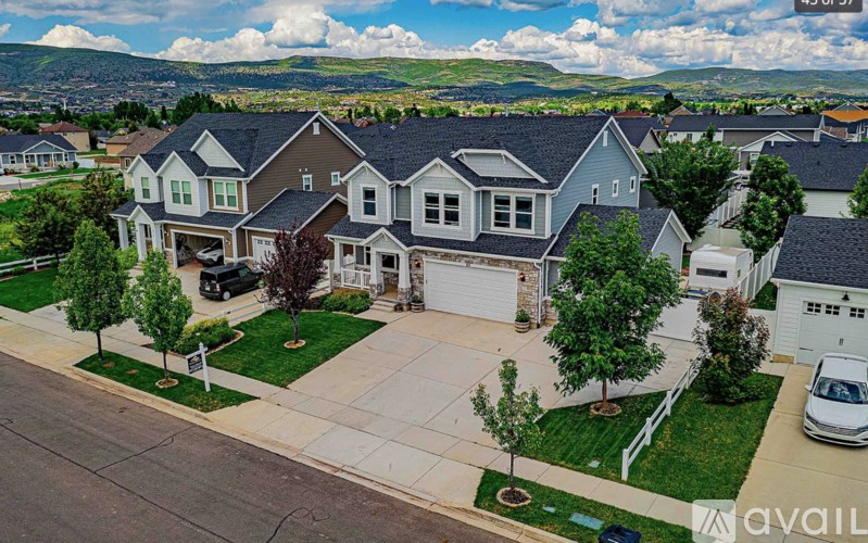 A large house with a garage is surrounded by a white fence and has a tree in front of it.