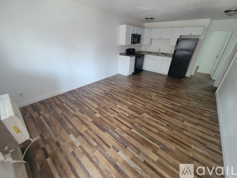 A room with wooden flooring and a black refrigerator.