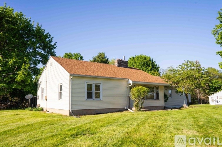 A house with a brown roof and a white exterior is surrounded by a green lawn.