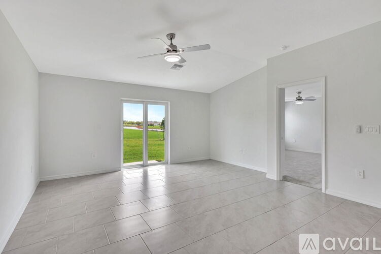 A spacious room with a ceiling fan and a view of a green lawn through a sliding glass door.