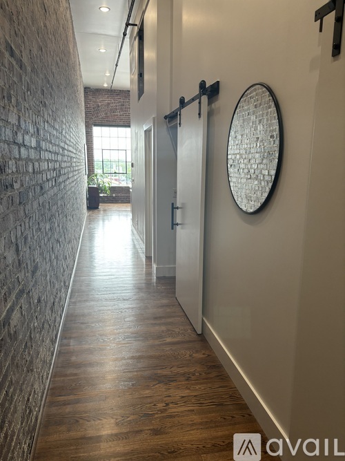 A long hallway with a brick wall on the left and a round mirror on the wall.