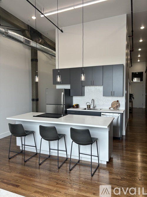 A modern kitchen with a white island and black chairs.