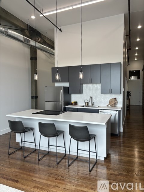 A modern kitchen with a white island and black chairs.