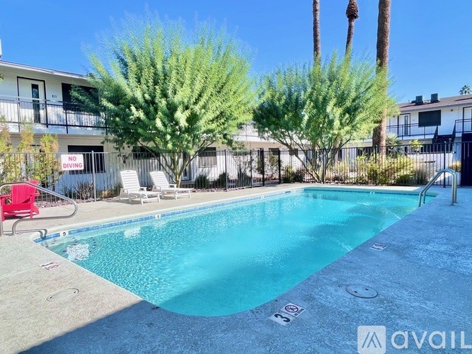 A pool surrounded by trees and chairs with a building in the background.